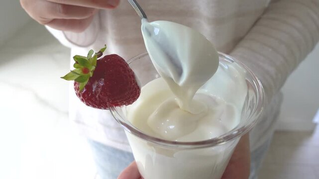Hands stirring strawberry yogurt in a glass with a spoon. Symbolizes probiotics, healthy eating, and the nutritional value of dairy products. Top view. Ideal for wellness, food, and lifestyle content