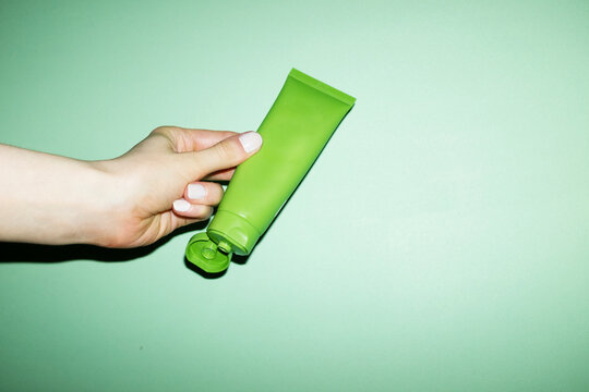 Hand holding a cosmetic beauty product green tube with lid with flash