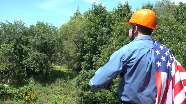 Construction worker in an orange hard hat with an American flag draped over his shoulder. Symbolizes American workers or Labor Day. Concept of pride in construction profession and American dream