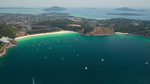 Nai Harn Beach in Phuket, Thailand, beautiful tropical coastline with turquoise water, sandy beach, and numerous sailboats anchored in the calm bay. Summer travel destination. Aerial view drone flight