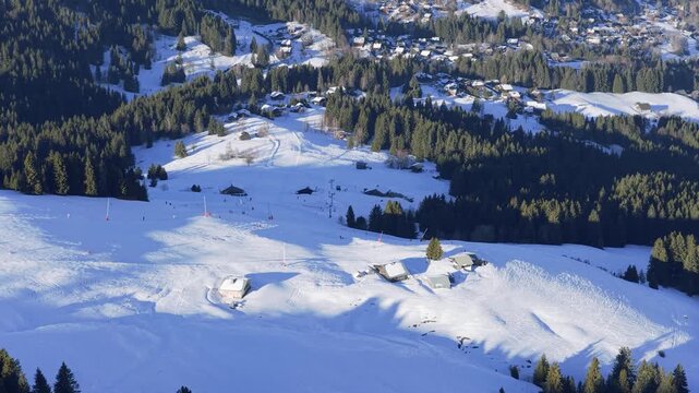 A wide aerial shot of the Megeve ski resort in the French Alps during winter. The footage shows snow-covered ski slopes, pine forests, scattered chalets, and a mountain village in the background