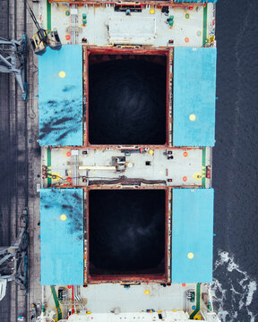 Aerial view of a cargo ship deck with large open hatches and industrial loading equipment in Riga, Latvia.