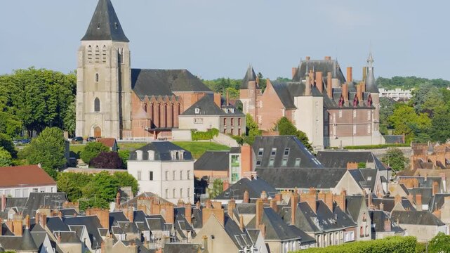 Daytime panoramic view of the historic town center of Gien, France, featuring the prominent church tower and the Chateau de Gien. The scene captures traditional French architecture with slate