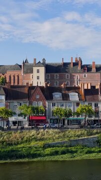 Daytime video showing picturesque historic buildings along the riverbank in Gien, France. The scene features classic French architecture with brick facades, gabled roofs, and a row of trees lining