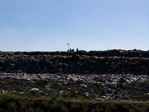 Aerial view of TPA Suwung landfill with piles of waste and workers under a clear blue sky in Kecamatan Denpasar Selatan, Bali, Indonesia.