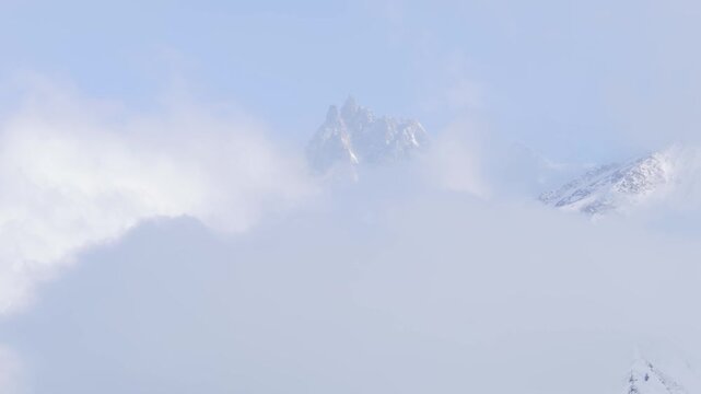 Timelapse of the iconic Aiguille du Midi mountain peak in the French Alps, partially obscured by drifting clouds. The snow-covered summit gradually becomes more visible as the mist shifts