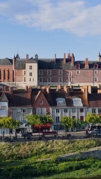 Daytime footage of the Chateau de Gien and traditional French houses along the Loire riverbank in Gien, Centre-Val de Loire, France. The video shows the iconic red brick chateau with its towers and