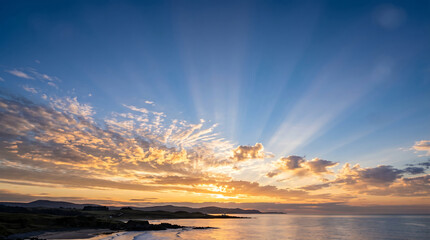 Fototapeta premium Scenic coastal sunset with dramatic sun rays over a tranquil ocean and lighthouse.