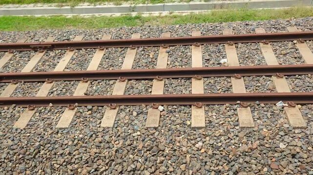 Industrial railway tracks passing by seen from moving train window with metal rails wooden sleepers and grey gravel ballast under bright daylight in rural area close to transport infrastructure line.