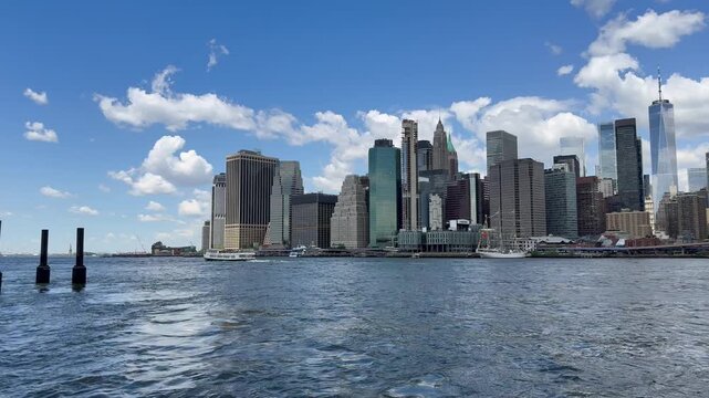 Panoramic, scenic view of Lower Manhattan. Financial district. Ferry, boat sails through the East River. Liberty Island in the background. Motion of cars traffic on FDR drive, road. New York City