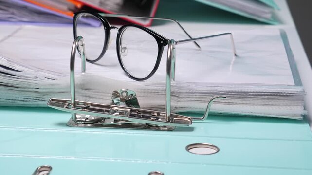 Office glasses resting on an open blue ring binder showcasing numerous organized clear plastic sleeves filled with important financial and business documents for accounting paperwork