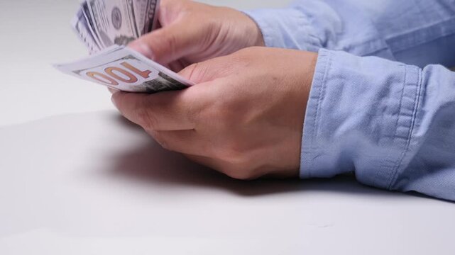 Person's hands carefully counting a stack of hundred dollar bills, representing financial transactions, wealth management, income, and budgeting on a clean white surface