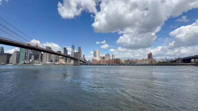 Panoramic, scenic view of Lower Manhattan skyline and Brooklyn Bridge. Motion of cars traffic on FDR drive. Financial district. Motion of East River waves. New York City, United States