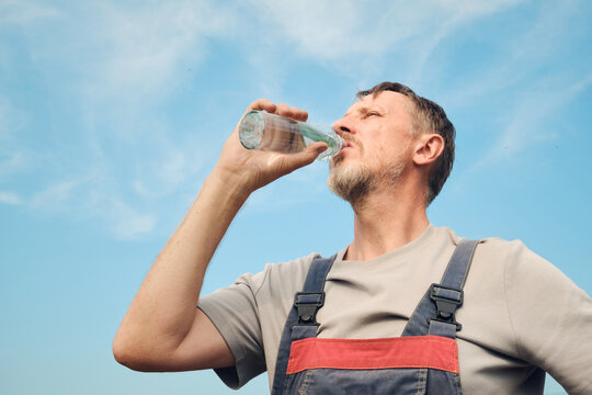Man in overalls hydrating during work break with blue sky background
