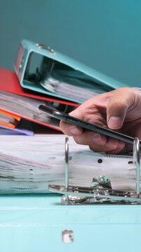 Vertical video person's hand holding a black smartphone. Connecting digital communication with physical binders and paper documents
