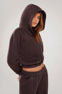 Portrait of a confident young woman wearing a trendy brown tracksuit  standing in a minimalist studio. Modern casual streetwear, athleisure fashion, comfortable outfit