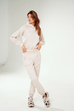 Fashionable young woman wearing a trendy tracksuit  standing in a minimalist studio. Modern casual streetwear, athleisure fashion, comfortable outfit, urban style