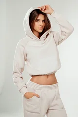 Portrait of a confident young woman wearing a trendy tracksuit  with hoodie standing in a minimalist studio. Modern casual streetwear, athleisure fashion, comfortable outfit © neonshot