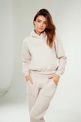 Portrait of a confident young woman wearing a trendy tracksuit  with hoodie standing in a minimalist studio.  © neonshot