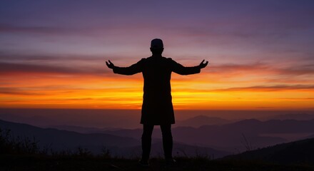Fototapeta premium Silhouette of Muslim man praying on mountain at sunrise. Person in worship with arms outstretched against colorful sky. Faith and spirituality concept