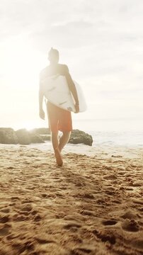 Surfer walking along the sandy beach at sunset, carrying a surfboard while wearing vibrant red shorts. Displaying determination and strength with a prosthetic leg, embracing the beauty of the ocean