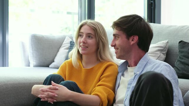 Beautiful young caucasian couple sitting on the floor in their living room, having an animated and happy conversation while enjoying their time together in their new modern apartment