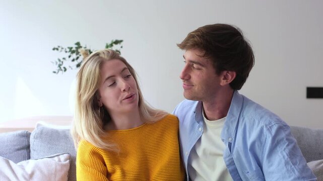 Loving young caucasian couple sitting together on a modern sofa in their living room, affectionately talking and gesturing while discussing their future plans and sharing ideas