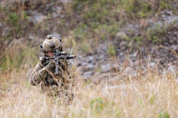 Fototapeta premium Soldier in military gear aims weapon while crouching in tall grass