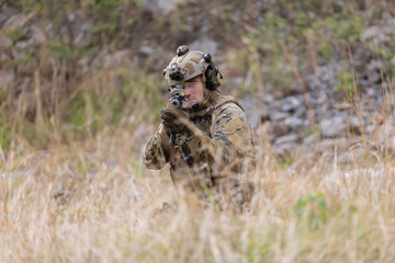Fototapeta premium Soldier in military gear aims weapon while crouching in tall grass