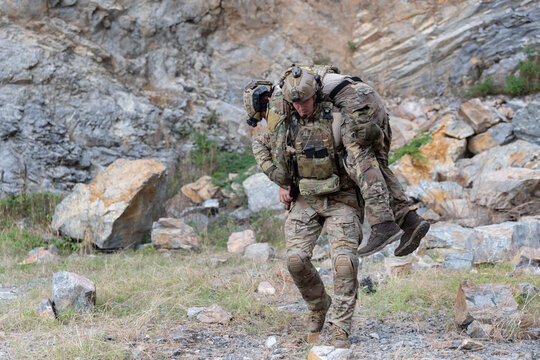 Soldier carries injured comrade over rocky terrain