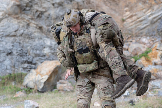 Soldier carries injured comrade over rocky terrain