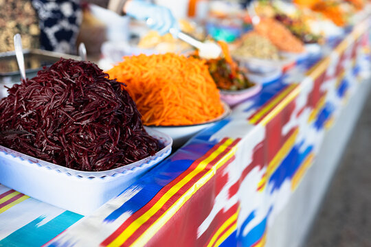 Shredded beetroot and carrot salads displayed at Siab bazaar in Samarkand on a colorful ikat tablecloth. Traditional Uzbek market food ideal for travel and cuisine content.