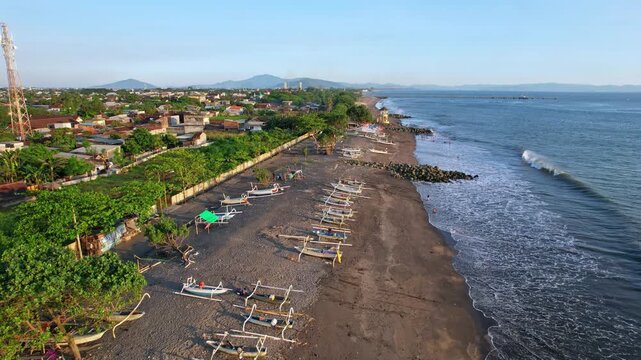 Aerial drone footage of the coastline of Mataram city, Lombok island, Indonesia, a beach with fishing boats, a rocky jetty with river, local houses, with a bay behind, at sunset