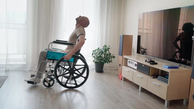 Disabled bald man in wheelchair stretching his upper body and neck in living room, handicapped person doing home rehabilitation exercise, physical therapy and health recovery concept