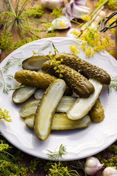 Pickled cucumbers with dill flowers, garlic, and horseradish, cut in half, on a plate, close-up. 