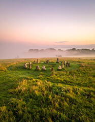 Fototapeta premium Morning mist rolls over a prehistoric stone circle standing in a lush green meadow within the English countryside landscape.