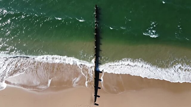 Aerial top view of ocean waves hitting sandy beach.