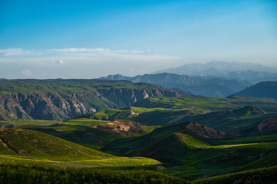 View of Arashan Lake surrounded by lush green rolling hills and rugged mountain ranges under a clear blue sky in Pop District, Namangan Region, Uzbekistan.