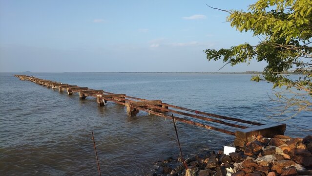 Rusty pier extends into calm body of water on sunny day