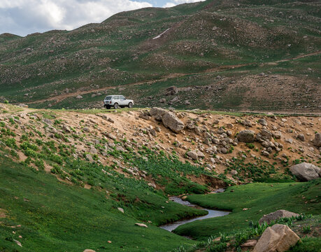 View of a white SUV parked on a grassy hill overlooking a small stream near Arashan Lake in Pop District, Namangan Region, Uzbekistan.