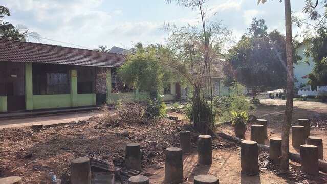 Sunlight illuminating a rural schoolyard with trees and wooden pillars