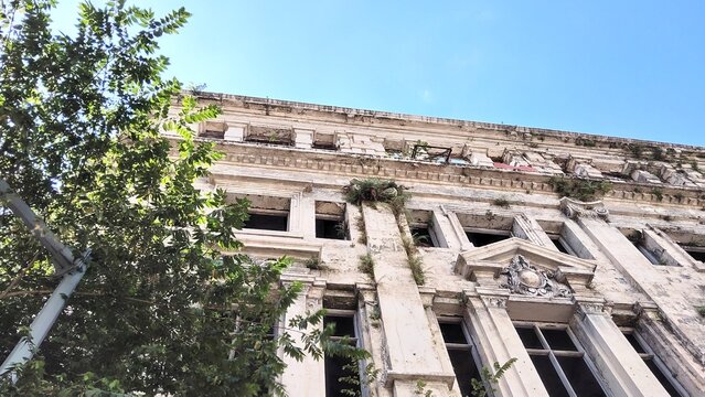 Low angle view of a weathered abandoned building with crumbling stone facade under a clear blue sky