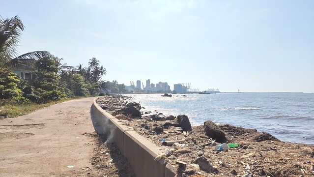 Coastal pathway along rocky shoreline with distant city skyline under clear sky