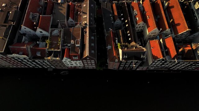 Drone camera glides above rows of historic canal houses with terracotta tiled roofs in an old Dutch city