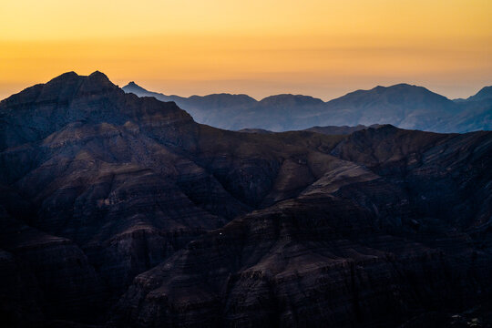 View of the rugged mountain range near Arashan Lake at golden hour with layered peaks and deep shadows in Pop District, Namangan Region, Uzbekistan.