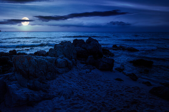huge stones on a sandy beach at night. wonderful summer vacation season at the black sea. full moon over calm waves washing the sand shore. mysterious nature background with cloudy sky