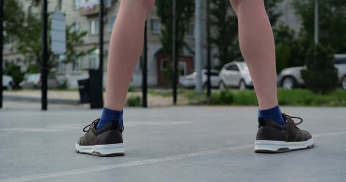 Close up of boy dribbling basketball on outdoor court in casual clothes. Focus on feet movement and bouncing ball during summer street basketball practice