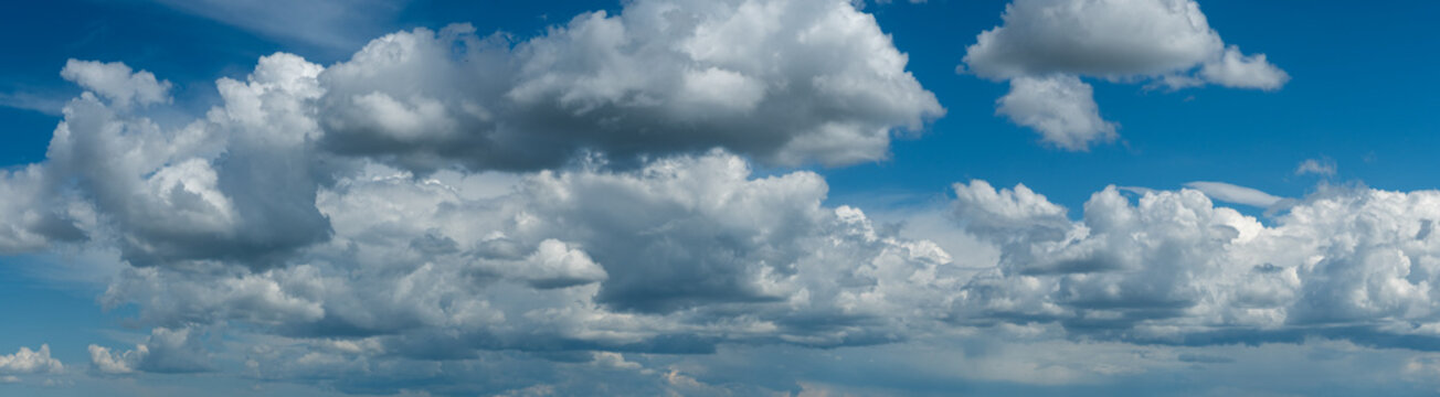 Panorama of a summer sky full of cumulus clods in shades of light blue, gray and white