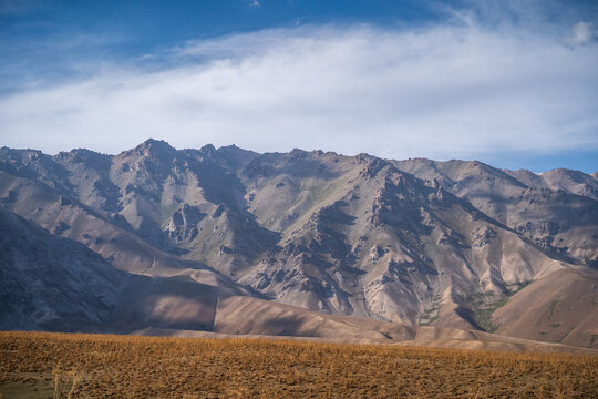 View of the rugged Arashan Lake mountain range with rocky slopes, sparse vegetation, and a clear blue sky in Pop District, Namangan Region, Uzbekistan.