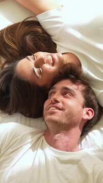 Happy affectionate young man and woman relaxing in bed together, smiling and enjoying a tender moment. Lovers sharing intimacy and connection while lying down in their peaceful bedroom